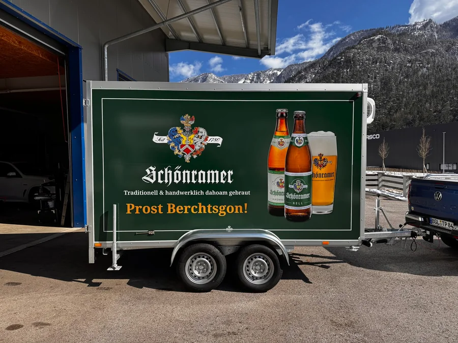 Beschrifteter Schönramer-Anhänger vor der Werkstatt und den Berchtesgadener Bergen
